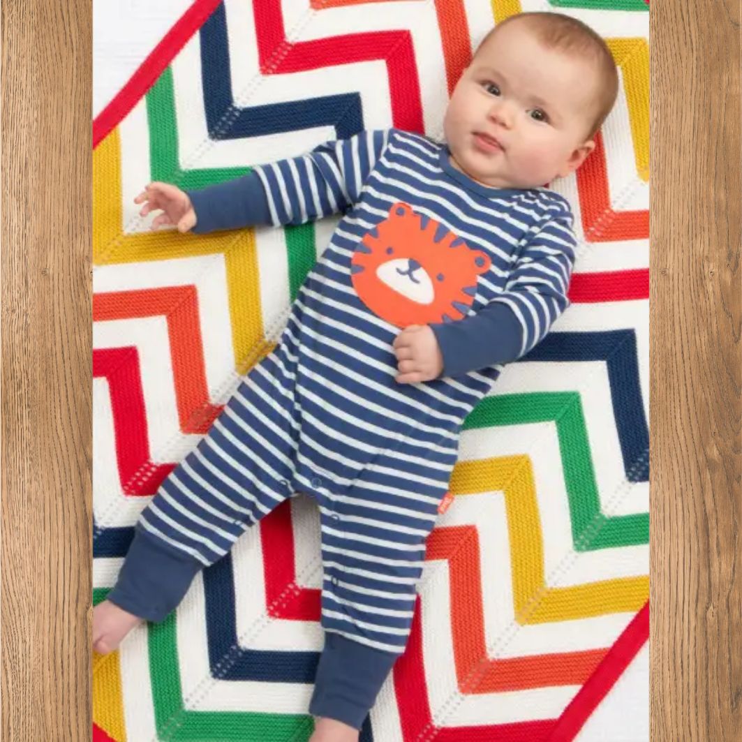 Baby wearing a blue and white striped onesie with a lion design on a colorful geometric-patterned rug.