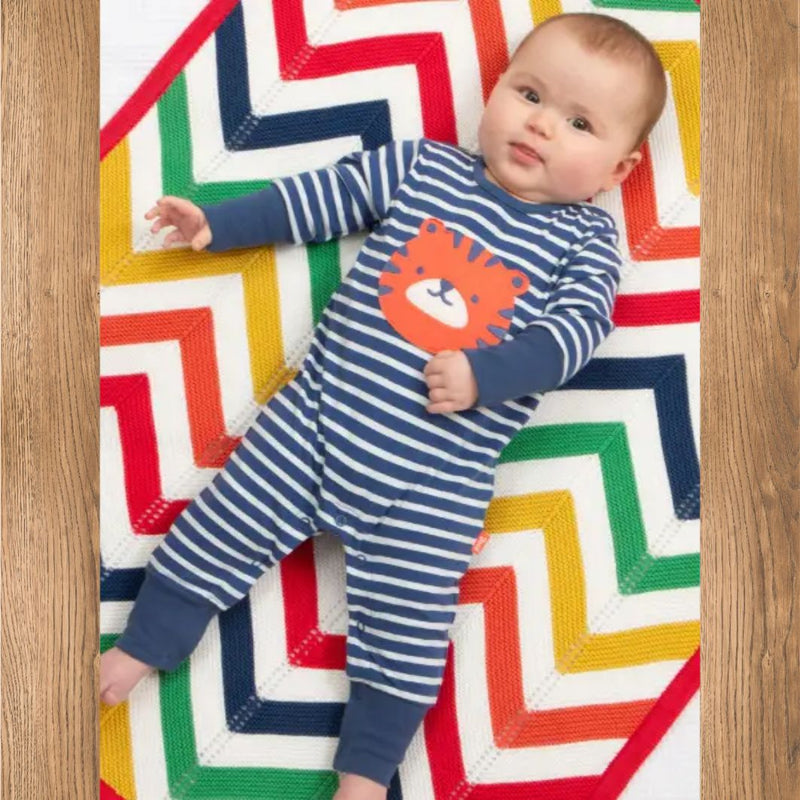 Baby wearing a blue and white striped onesie with a lion design on a colorful geometric-patterned rug.